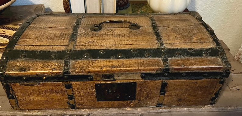 May include: A wooden chest with a hinged lid, black metal accents, and a brass handle. The chest has a dark wood finish and is decorated with metal studs.