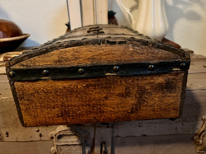 May include: A wooden box with a dark brown stain and black metal trim. The box has a curved top and is decorated with metal studs.