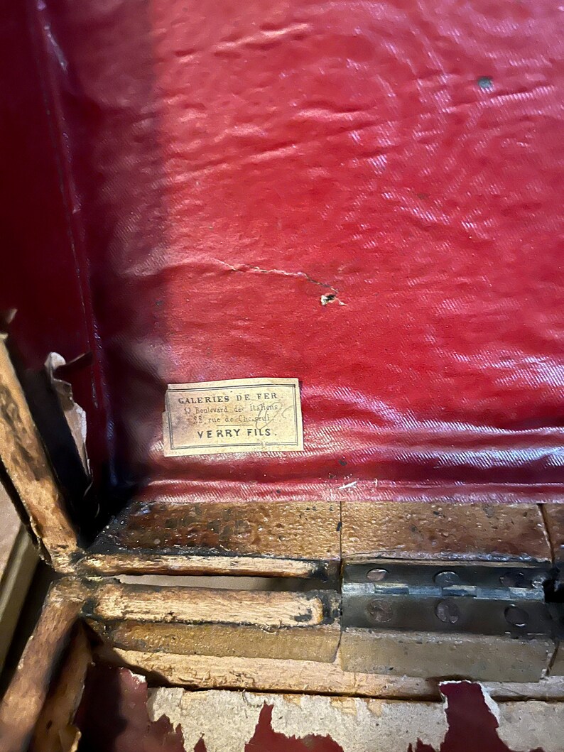 May include: Close-up of a red fabric-covered wooden box with a label that reads "Galeries De Fer, 6 Boulevard St. Martin, 35 rue de Charenton, VERRY FILS."