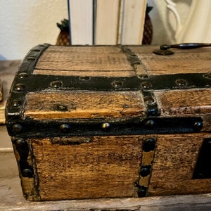 May include: A small wooden box with a black leather trim and metal studs. The box has a hinged lid and a brass handle.