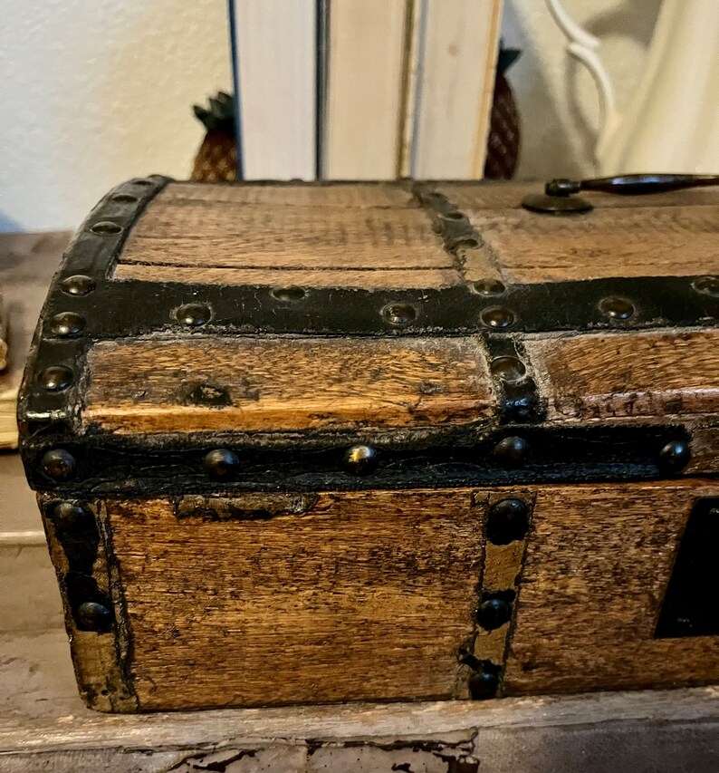 May include: A small wooden box with a black leather trim and metal studs. The box has a hinged lid and a brass handle.
