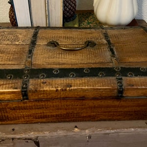 May include: A wooden chest with a brass handle and black metal accents. The chest has a distressed finish and is made of wood.