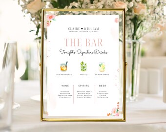 May include: A gold-framed sign with a white background and pink floral accents. The sign reads "The Bar" and lists the signature drinks for the wedding of Claire and William on October 14th, 2023. The drinks include an Old Fashioned, a Mojito, and a Lemon Spritz. The sign also lists the wine, spirits, and beer options available.