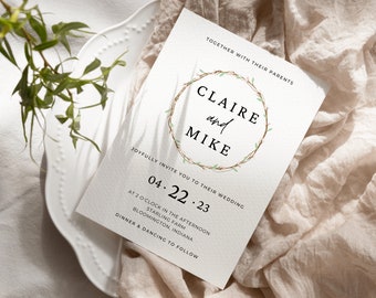May include: Wedding invitation with a white background and a brown and green wreath with the text "Claire and Mike" in the center. The date of the wedding is "04.22.23" and the location is "Starling Farm, Bloomington, Indiana".