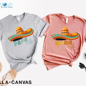 Puede incluir: Dos camisetas grises y rosas con un dise&ntilde;o de sombrero colorido y el texto "Papa cita" y "Mama cita" impreso en ellas.