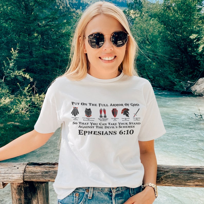 Puede incluir: Camiseta blanca con un gr&aacute;fico negro y rojo de la armadura completa de Dios. El texto dice "Ponte la armadura completa de Dios, para que puedas resistir los planes del diablo, Efesios 6:10".