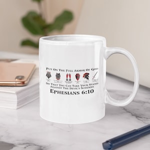 Puede incluir: Taza de cer&aacute;mica blanca con un dise&ntilde;o en negro y rojo. La taza presenta una cita de la Biblia, Efesios 6:10, "Rev&iacute;stanse de toda la armadura de Dios, para que puedan hacer frente a las estrategias del diablo."