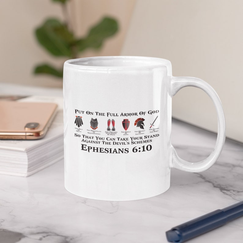 Puede incluir: Taza de cer&aacute;mica blanca con un dise&ntilde;o en negro y rojo. La taza presenta una cita de la Biblia, Efesios 6:10, "Rev&iacute;stanse de toda la armadura de Dios, para que puedan hacer frente a las estrategias del diablo."
