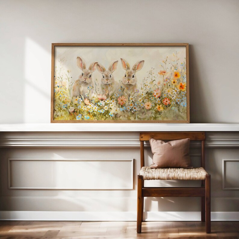 May include: A framed watercolor painting of three brown rabbits sitting in a field of colorful wildflowers. The rabbits are looking at the viewer. The background is a soft, light blue.