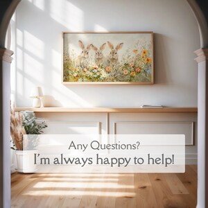 May include: A framed painting of three brown rabbits sitting in a field of colorful flowers. The painting is hanging on a white wall in a hallway with a wooden floor.