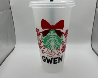 May include: A white reusable cup with a green Starbucks logo, a red bow, and red snowflakes. The cup has the name "GWEN" printed on the bottom.