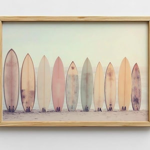 May include: A framed print of a row of 10 surfboards in various shades of pink, blue, and green, lined up on a sandy beach.