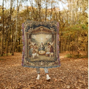 May include: A woven tapestry throw blanket featuring a traditional nativity scene with Mary, Joseph, and baby Jesus in a stable with animals. The tapestry is framed with a dark brown border and has a fringe.