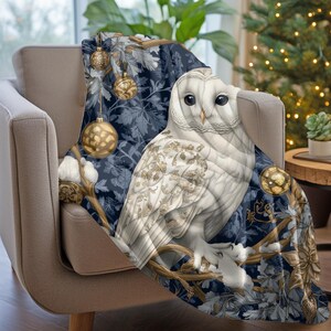 May include: A white owl with gold accents sits on a branch with blue and gold ornaments. The owl is surrounded by a blue and gold floral pattern. The throw blanket is perfect for adding a touch of whimsy to your home decor.