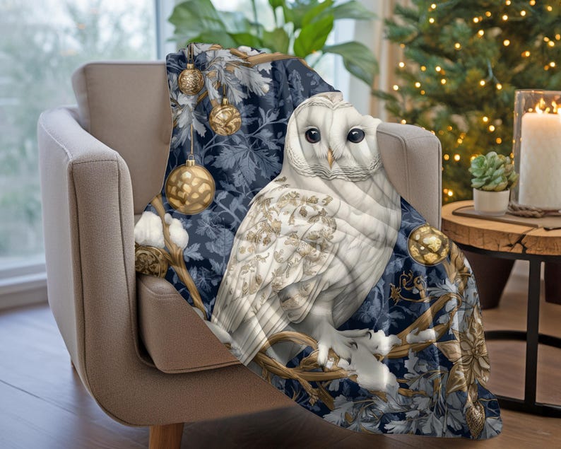 May include: A white owl with gold accents sits on a branch with blue and gold ornaments. The owl is surrounded by a blue and gold floral pattern. The throw blanket is perfect for adding a touch of whimsy to your home decor.