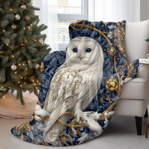 May include: A white owl with gold accents sits on a branch with blue and gold leaves. The owl is surrounded by gold ornaments and a blue background. The owl is a throw blanket.
