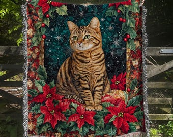 May include: A woven throw blanket featuring a tabby cat surrounded by poinsettias, holly, and berries. The background is a dark teal with snowflakes. The blanket has a fringed edge and is suitable for indoor use.