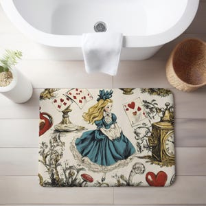 May include: A white bath mat with a whimsical Alice in Wonderland design. The mat features a blue and white dress, playing cards, a pocket watch, and a red heart.