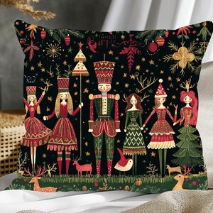 May include: Decorative square pillow with a black background featuring a festive design. The design includes illustrations of nutcrackers, deer, and figures in red and green outfits, with gold accents. A Christmas-themed pillow.