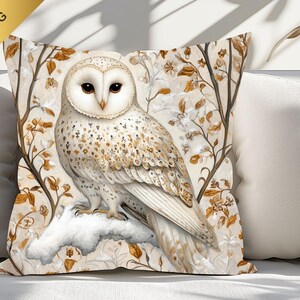 May include: A white and brown owl with gold accents sits on a branch with white snow and brown leaves. The owl is perched on a branch with a white background.