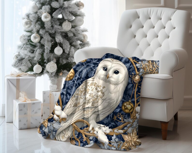 May include: A white owl with gold accents sits on a blue and gold throw blanket with a wintery forest scene. The blanket is draped over a white armchair.