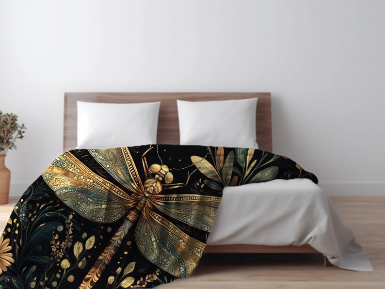 May include: A black blanket with a large, detailed dragonfly design in gold and green. The dragonfly is the focal point, with intricate wing patterns. The blanket is draped over a bed with white bedding, creating a striking contrast.