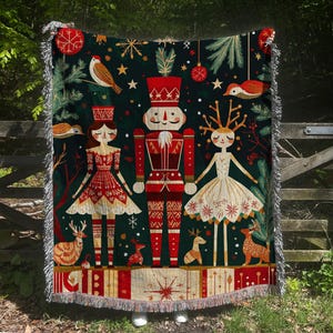 May include: A woven tapestry throw blanket features a Nutcracker, two dancers, and a variety of festive details. The design is set against a dark green background with red, white, and gold accents.