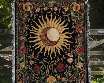 May include: A tapestry throw blanket with a dark background featuring a large gold sun with a crescent moon inside. The sun and moon are surrounded by a floral design with red, yellow, and green flowers.