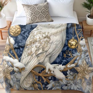 May include: A white owl with gold accents sits on a branch with gold ornaments and blue and white floral designs. The owl is perched on a branch with snow-covered branches and leaves.