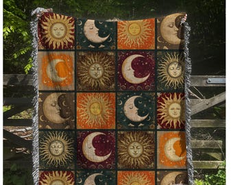 May include: A woven throw blanket featuring a repeating pattern of suns and crescent moons in shades of orange, teal, and burgundy. The celestial design is displayed in a grid format, with a fringed edge.