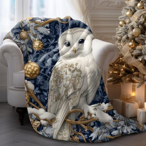 May include: A blue and white throw blanket with a snowy owl design. The owl is perched on a branch with gold ornaments and snowflakes.