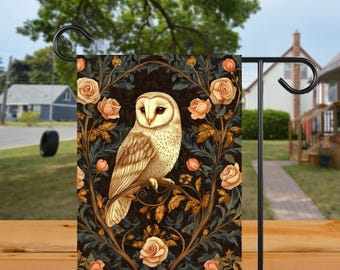 Puede incluir: Una bandera de jardín con una ilustración detallada de un búho común posado en una rama, rodeado de rosas y follaje. El búho tiene una cara blanca y plumas marrones, sobre un fondo oscuro. La bandera se muestra en un soporte de metal negro.
