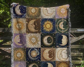 May include: A tapestry throw blanket with a repeating pattern of suns and moons. The suns are yellow with a human face and the moons are white with a human face. The background is a patchwork of blue, green, purple, and yellow.