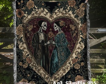 May include: Woven throw blanket featuring a heart-shaped design with a skeleton couple holding hands. The blanket has a floral border and fringe. The text "Art Studio 905" and "Original Art Woven Throws" are visible.