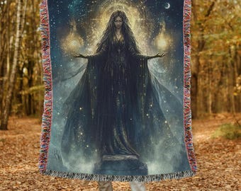 May include: A woven tapestry throw blanket featuring a dark-haired woman in a long black gown standing on a stone platform. The woman is surrounded by a swirling galaxy of stars and light. The blanket has a fringe border.