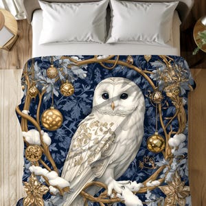 May include: A white owl with gold accents sits on a branch with gold ornaments hanging from it. The background is a dark blue with a wintery feel.