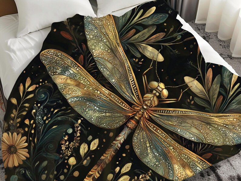 May include: A decorative blanket featuring a detailed illustration of a dragonfly with intricate wing patterns in shades of gold, teal, and brown. The dragonfly is set against a dark background with floral and leaf accents, creating a nature-inspired design.