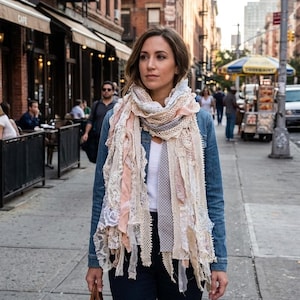 May include: A multi-textured scarf featuring a blend of cream, beige, and soft pink fabrics. The scarf incorporates various lace patterns, frayed fabric strips, and a grey polka-dot section, layered to create a voluminous, fringed appearance.