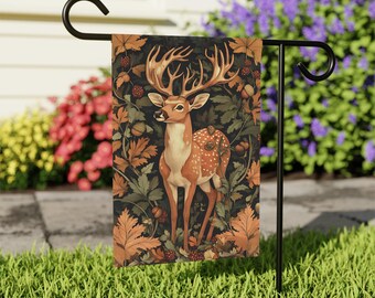 May include: A garden flag with a detailed illustration of a deer with large antlers, set against a backdrop of autumn leaves and foliage. The deer has a spotted coat and is surrounded by acorns and berries. The flag is displayed on a black metal stand.