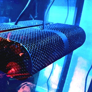 May include: A black metal microphone with a hexagonal mesh grille, suspended from a blue and white background.