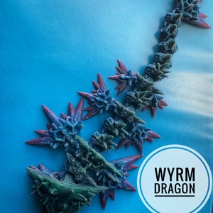 May include: A 3D printed blue and green wyrm dragon with red accents. The dragon is posed in a curled position with its head facing the viewer. The text "WYRM DRAGON" is written in white on a white circle.