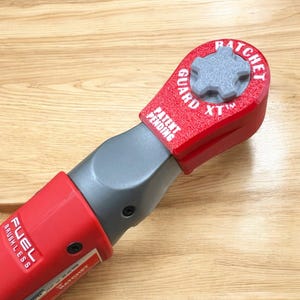 Könnte beinhalten: Rotes und graues Akku-Werkzeug mit rotem Ratschen-Schutz, beschriftet mit "Ratchet Guard XT" und "Patent Pending". Das Werkzeug ist mit "Fuel Brushless" gekennzeichnet.