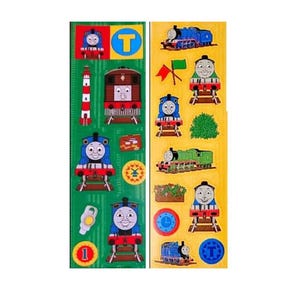 May include: Two vertical sticker sheets featuring Thomas the Tank Engine characters and motifs. The left sheet is green with blue trains, a lighthouse, and a number one. The right sheet is yellow with various green and blue trains, flags, and a clock.