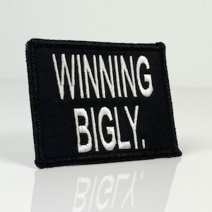 Puede incluir: Parche bordado negro con texto blanco que dice "Winning Bigly."