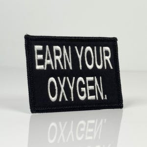 Puede incluir: Parche bordado negro con texto blanco que dice "Earn Your Oxygen."