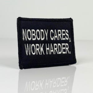 Peut inclure: Écusson brodé noir avec du texte blanc qui dit "Nobody Cares, Work Harder."