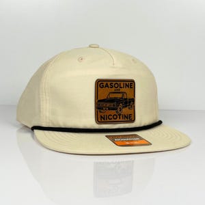 May include: A beige baseball cap with a black brim and a brown leather patch that says "Gasoline and Nicotine" with a black silhouette of a pickup truck. The patch is on the front of the cap.