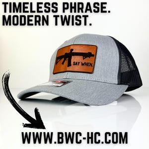 May include: A gray and black trucker hat with a brown leather patch featuring a silhouette of a rifle and the text "Say When."