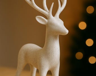 May include: A decorative, off-white deer figurine with detailed antlers. The deer is standing on a wooden surface, with a blurred background that includes a Christmas tree with bokeh lights. The figurine is a festive home decor item.