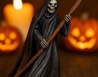 May include: A figurine of the Grim Reaper, a skeletal figure in a black hooded cloak, holding a scythe. The figure is on a black base. The background includes a lit candle and jack-o'-lanterns, suggesting a Halloween theme.